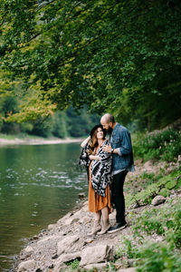 Rear view of couple standing against trees at shore