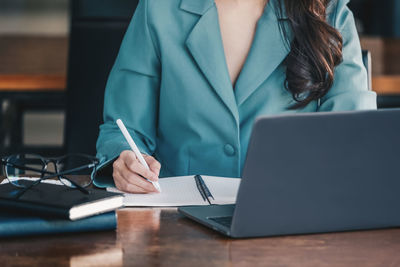 Midsection of businesswoman using laptop on table