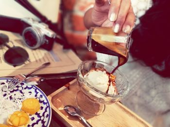 Midsection of woman pouring chocolate sauce on ice cream at table