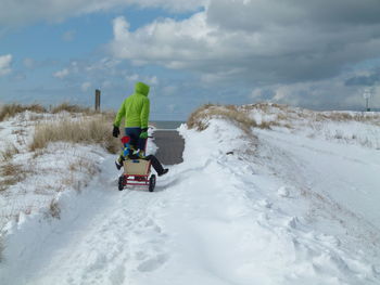 Rear view of father pulling cart with child on snow