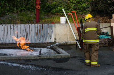 Rear view of firefighter extinguishing fire by retaining wall