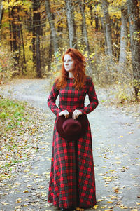 The red-haired girl in red dress walking in autumn park.