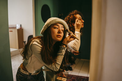 Young female friends doing make-up at home