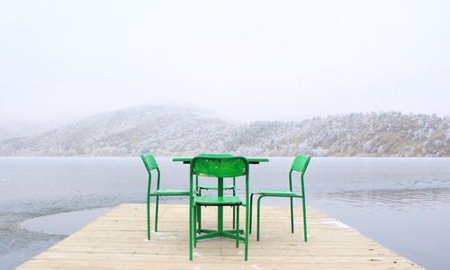 Table and chairs on pier by lake during winter