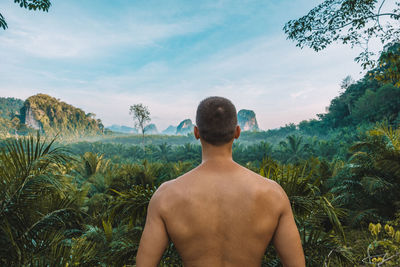 Rear view of shirtless man standing on field against sky