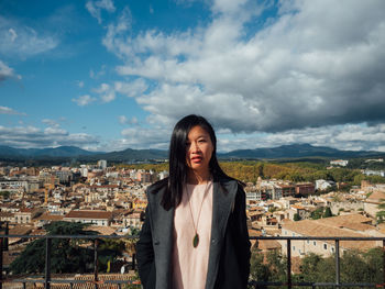 Portrait of young woman standing against buildings in city