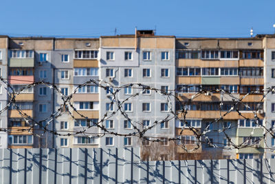 Residential multi-storey building behind a fence with barbed wire at daylight