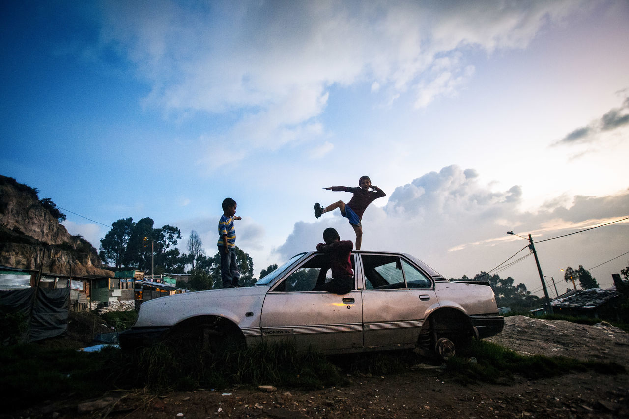 mode of transportation, sky, car, transportation, cloud - sky, motor vehicle, land vehicle, nature, damaged, abandoned, day, outdoors, obsolete, decline, incidental people, garbage, deterioration, run-down, real people, junkyard