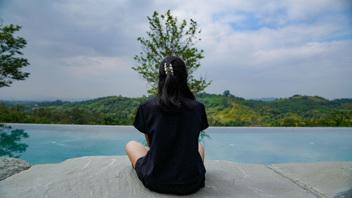 Rear view of woman sitting by tree against sky