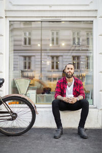 Portrait of smiling owner with coffee sitting outside candy store