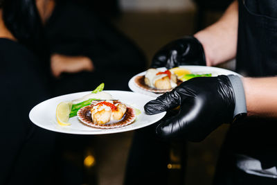 Close-up of waiter's hands in black gloves serving scallops. two portions of haute cuisine, catering