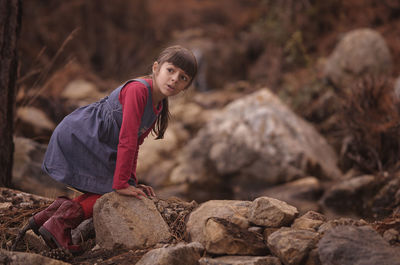 Girl looking away while keeling on rock