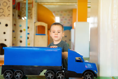 A little toddler boy plays with a big blue car in a children's entertainment center.