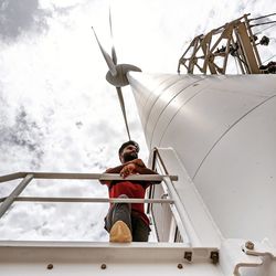 Low angle view of man standing on wind turbine
