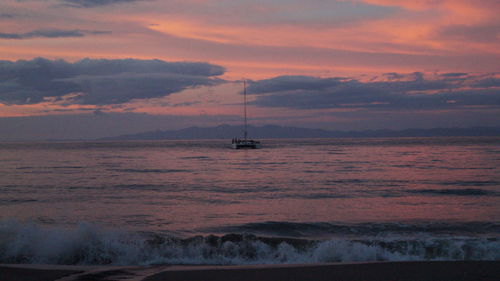 Sailboat sailing in sea against sunset sky