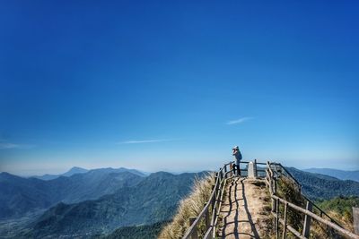 Mid distance view of woman photographing while standing at observation point against blue sky