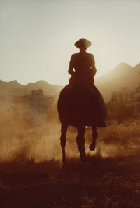 Silhouette man riding horse on field against clear sky during sunset