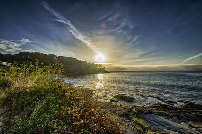 Scenic view of beach against cloudy sky during sunset