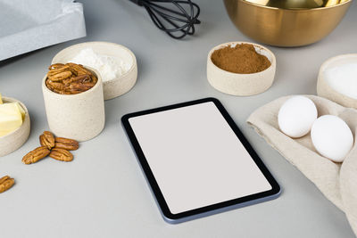 Digital touch screen tablet with brownie recipe ingredients and kitchen utensils on gray background.