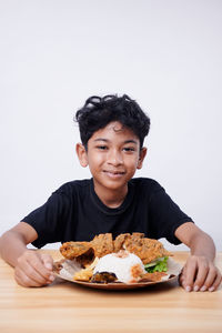 Portrait of young woman having food on table against white background