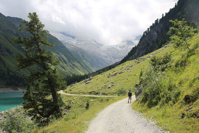 Rear view full length of man walking on dirt road against mountains