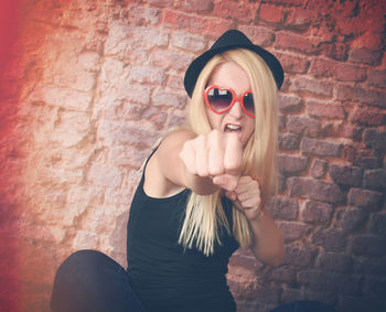 Portrait of young woman wearing sunglasses standing against brick wall