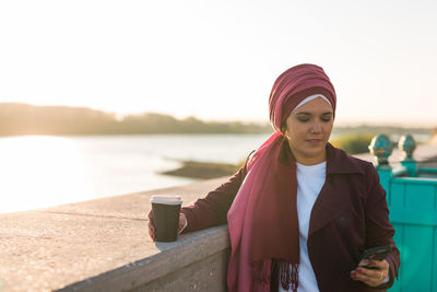 Portrait of young woman standing against lake