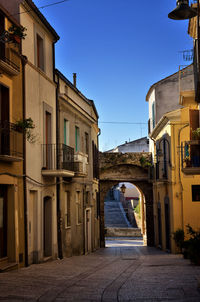 Empty road amidst buildings against clear blue sky