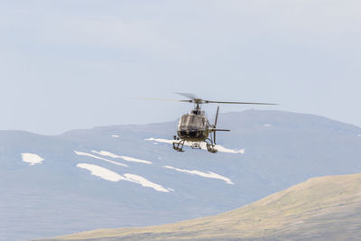 Low angle view of helicopter flying in mountains against clear sky