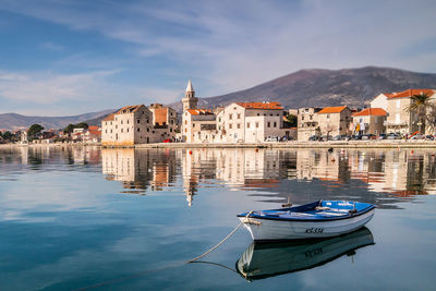 Boats moored on river by buildings in city against sky