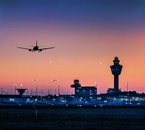 Airplane flying by illuminated airport against sky at dusk