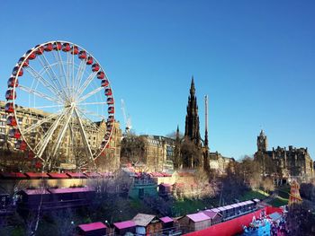 Ferris wheel by historic scott monument in city against clear sky