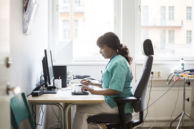 Side view of woman using phone while sitting on table