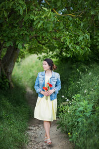 Woman in yellow dress gathering poppy and wildflowers, walking in summer meadow