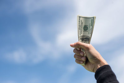 Close-up of woman holding us paper currency against sky