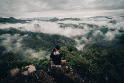 Woman sitting on mountain against sky