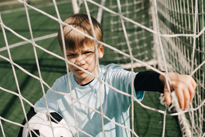 Portrait of boy with arms raised against fence