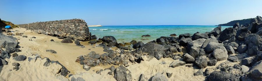 Panoramic view of rocks on beach against clear blue sky