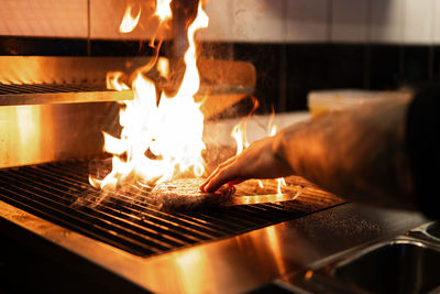 Crop anonymous male chef grilling tasty patty while preparing burgers in kitchen of restaurant