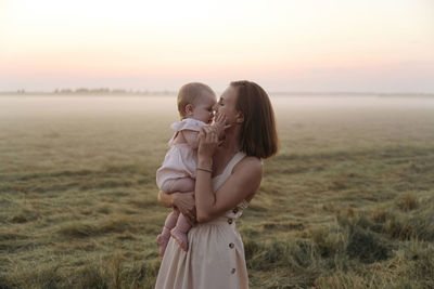 Mother carrying cute daughter at field during sunset