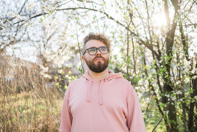 Portrait of young man wearing sunglasses standing against trees