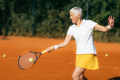 Smiling mature woman playing tennis in summer