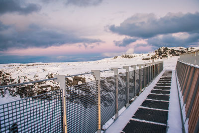 Fence by railing against sky during winter