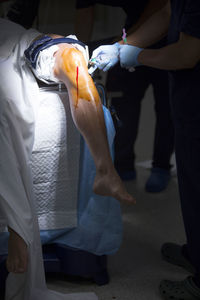 Low section of doctor injecting syringe on patient leg in operating room