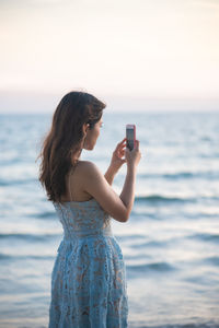 Young woman using mobile phone in sea against sky