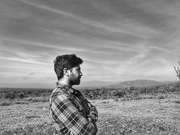 Side view of man looking away while standing on land against sky