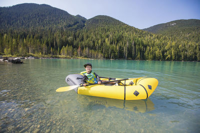 Young boy paddling yellow packraft boat on scenic lake near whistler.