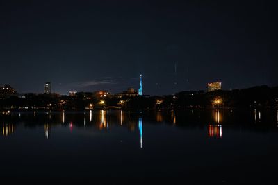 Illuminated city by river against sky at night