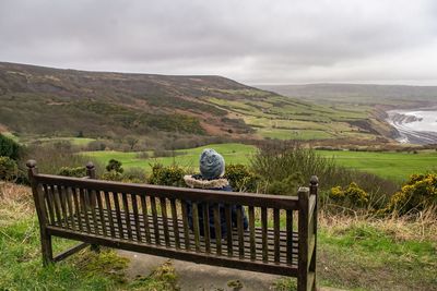 Woman sitting on bench against mountains