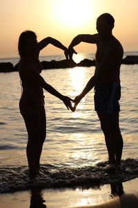 Silhouette couple standing at beach during sunset